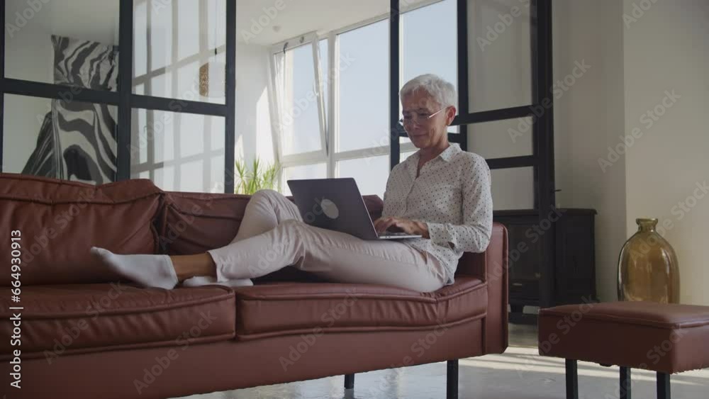Mature Woman Browsing on Laptop on Sofa in Office Mature Woman Browsing on Laptop on Sofa in Office