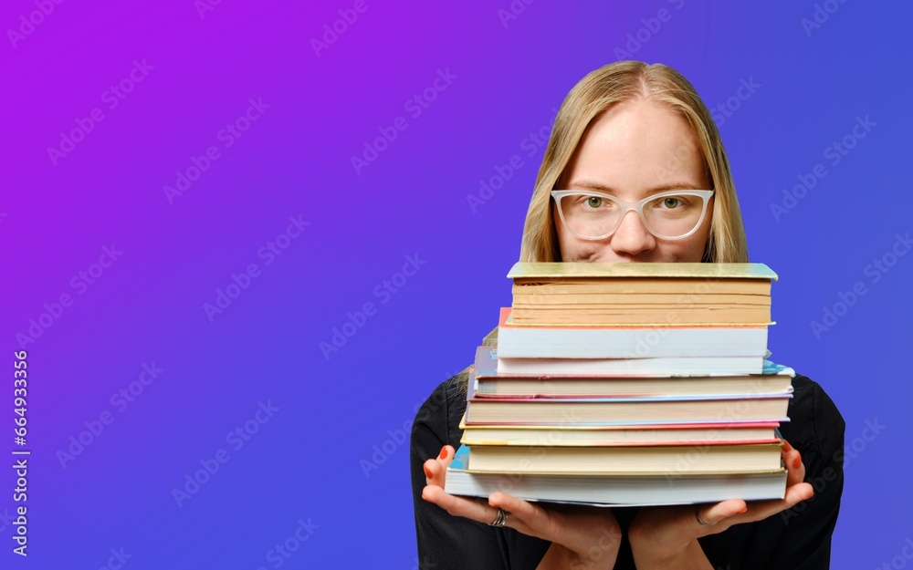 Caucasian female student in glasses holds a lot of books in her hands on a purple background. Book Lovers Day. Caucasian female student in glasses holds a lot of books in her hands on a purple background. Book Lovers Day.