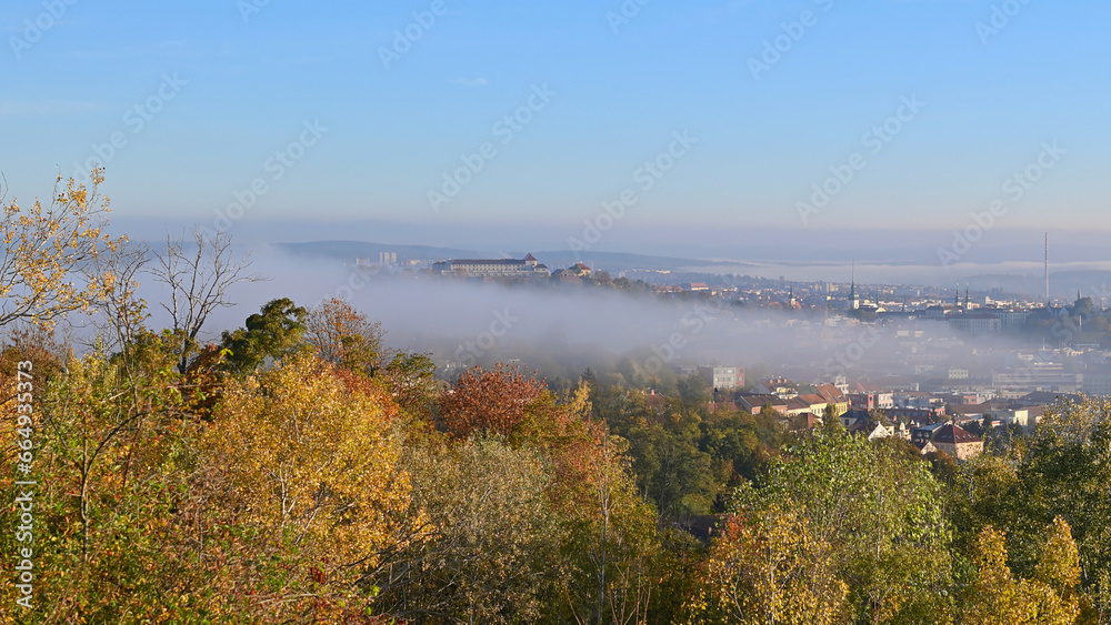 The city of Brno, Czech Republic, shrouded in morning fog. View from the hill above the town at autumn sunrise.