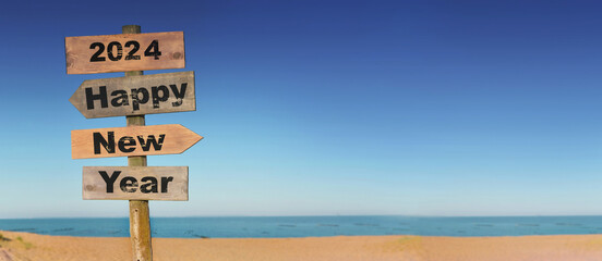 2024 happy new year written on a direction sign in front of a beach on blue sky