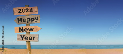 2024 happy new year written on a direction sign in front of a beach on blue sky