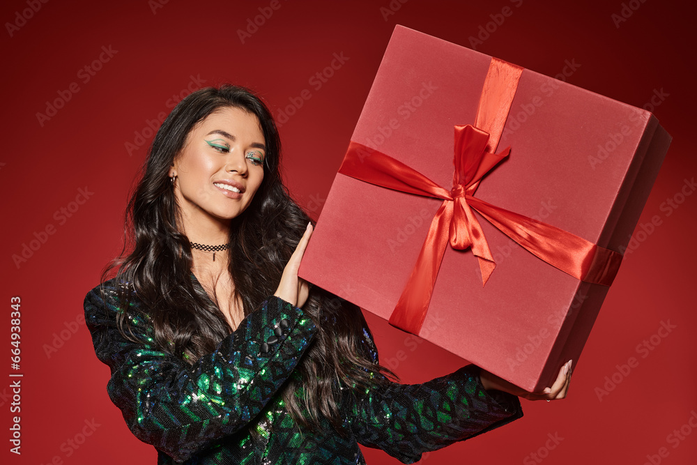 happy asian woman in green jacket with sequins holding present on red backdrop, Merry Christmas happy asian woman in green jacket with sequins holding present on red backdrop, Merry Christmas