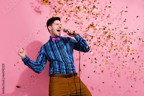 Portrait of carefree handsome guy arm hold wired microphone shout sing flying confetti isolated on pink color background photo