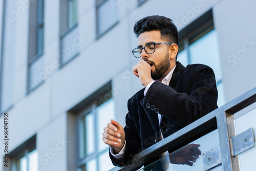Tired exhausted Indian businessman yawning, sleepy inattentive feeling somnolent lazy bored gaping suffering from lack of sleep, falling asleep outdoors. Arabian Hindu freelancer guy in downtown city