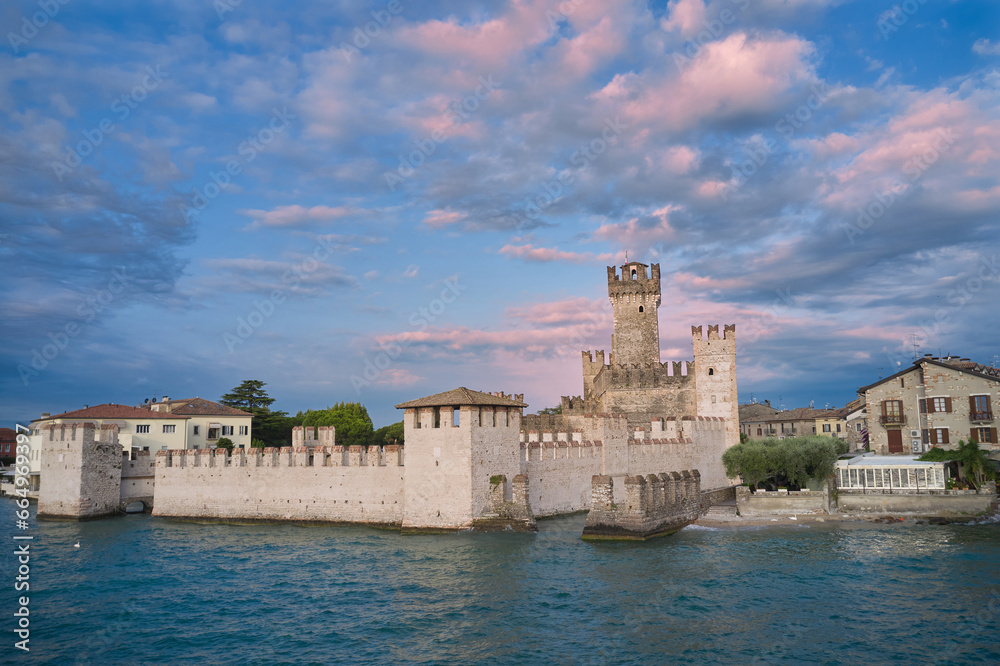 Sirmione at sunrise. Scaliger Castle Sirmione on Lake Garda in Italy. Morning view of Scaliger Castle Sirmione. Pink clouds over Scaliger Castle.