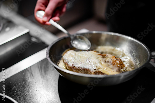 Professional chef cooking beef steak in frying pan on stove in restaurant kitchen