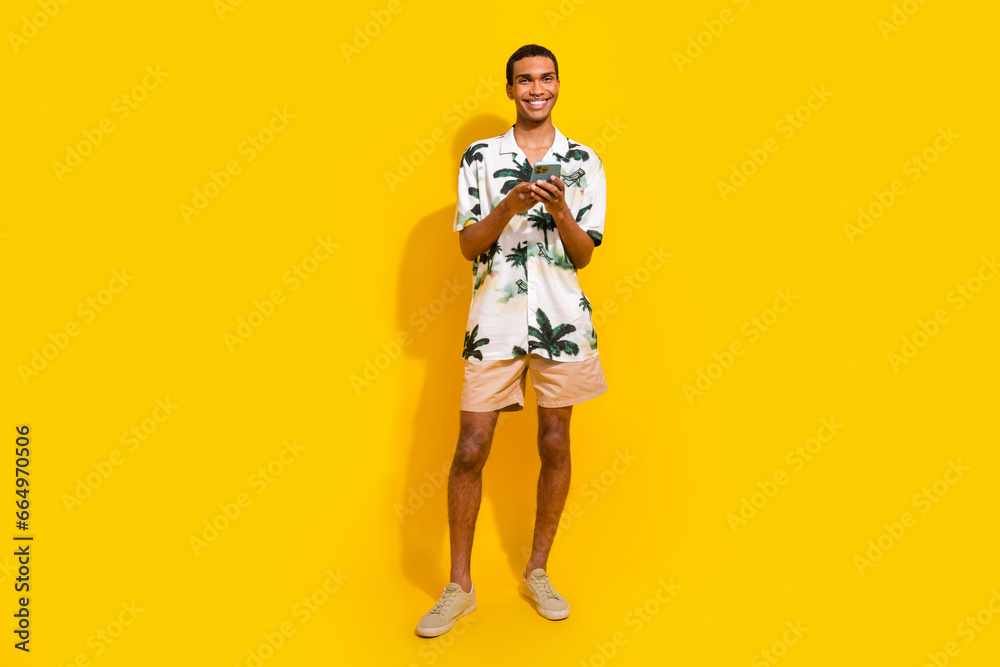 Full size photo of handsome young guy hold device ecommerce promo wear trendy palms print outfit isolated on yellow color background Full size photo of handsome young guy hold device ecommerce promo wear trendy palms print outfit isolated on yellow color background