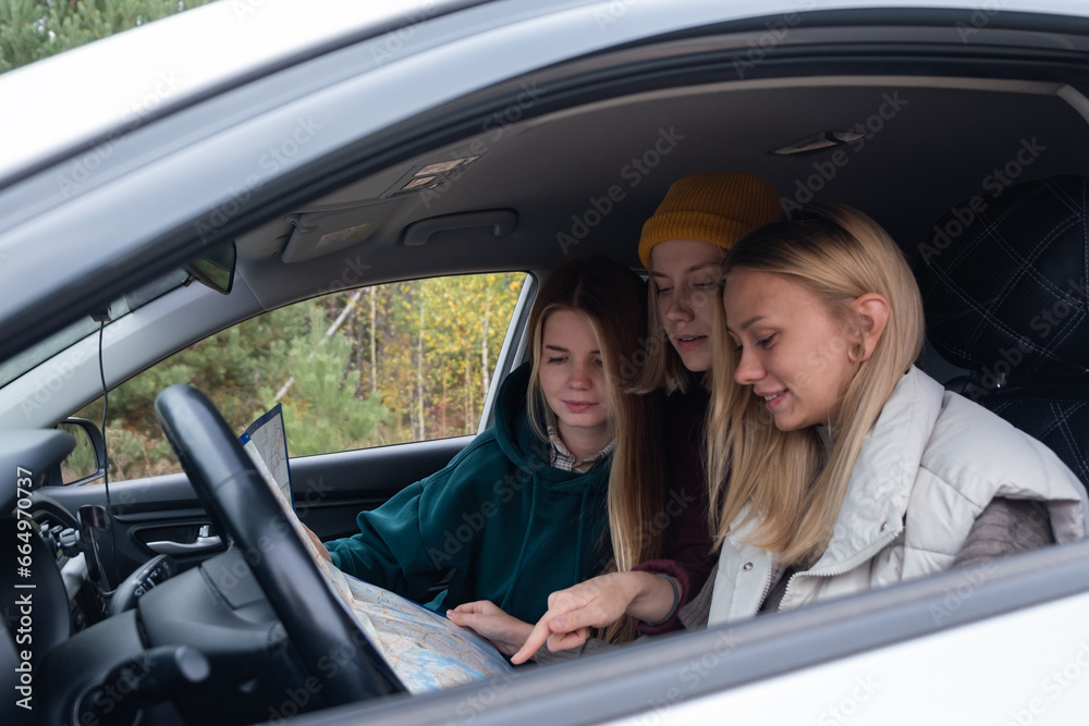 Three girls are reading a map. Friends are traveling by car in the forest.