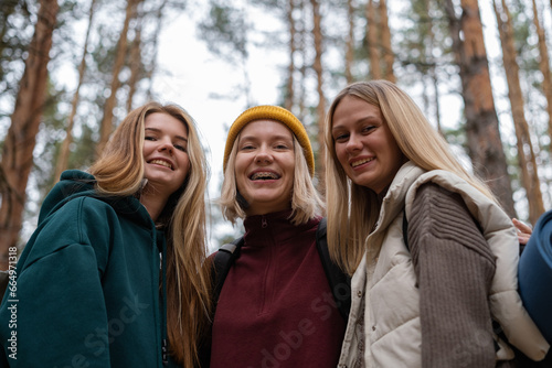 The girls travel on foot through an autumn forest. Happy camper friends walking along the dirt road to the campsite © deine_liebe