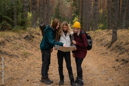 Three young women reading a map in the fall woods. The friends travel on foot through the forest, navigating the map © deine_liebe