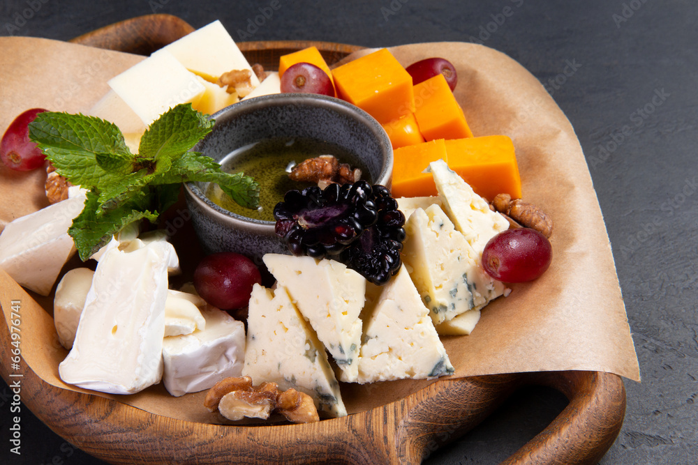 Assorted cheeses in a wooden plate. On a dark background. Assorted cheeses in a wooden plate. On a dark background.