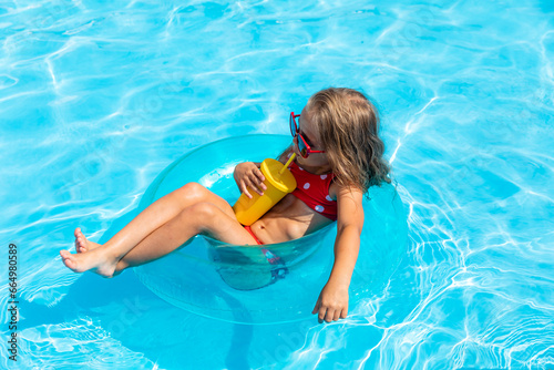 Pretty little girl swimming in outdoor pool and have a fun with inflatable circle and drinking lemonade