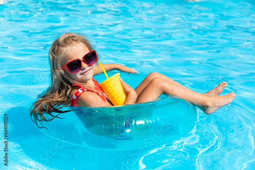 Pretty little girl swimming in outdoor pool and have a fun with inflatable circle and drinking lemonade