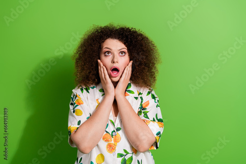 Photo of impressed speechless person arms touch cheekbones open mouth look up empty space isolated on green color background