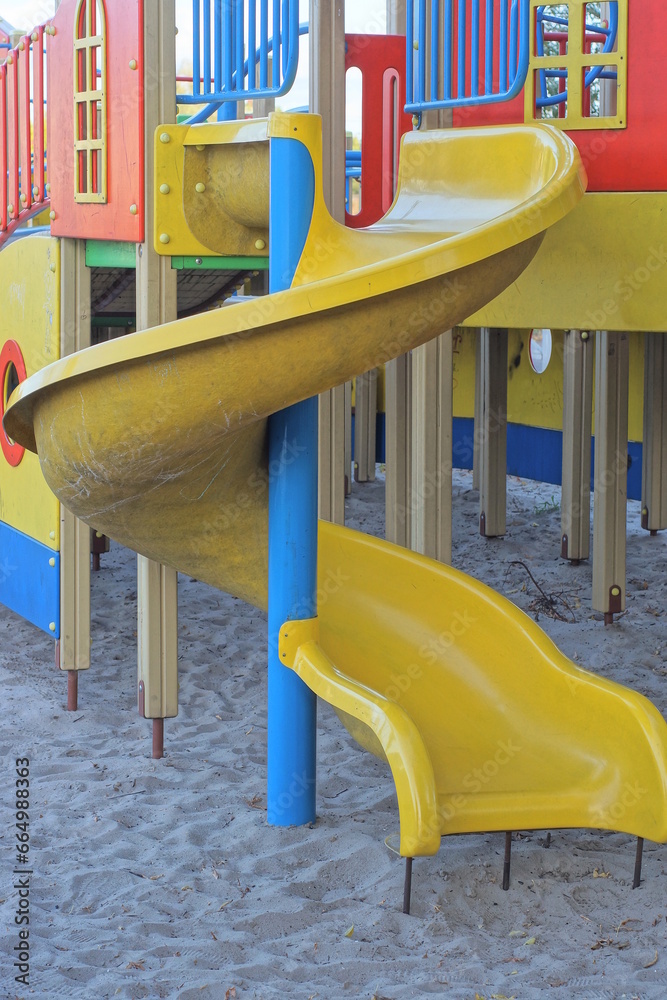 yellow plastic slide on a playground on gray sand outdoors