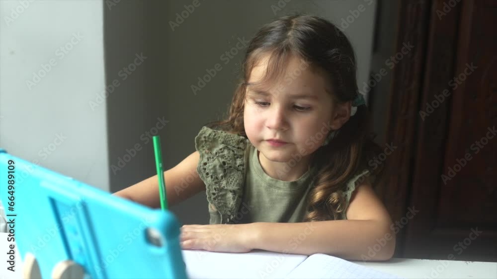 Little girl studying at home taking classes online on her tablet and making exercises and homework. High quality FullHD footage Little girl studying at home taking classes online on her tablet and making exercises and homework. High quality FullHD footage