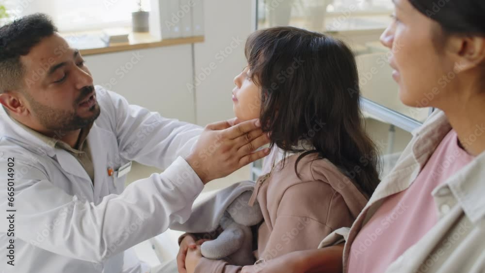 Waist up of careful Middle Eastern male child otolaryngologist examining neck of little Hispanic girl for swollen glands Waist up of careful Middle Eastern male child otolaryngologist examining neck of little Hispanic girl for swollen glands