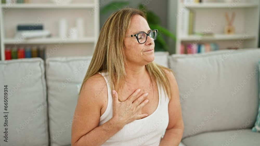 Middle age hispanic woman sitting on sofa suffering heart attack at home