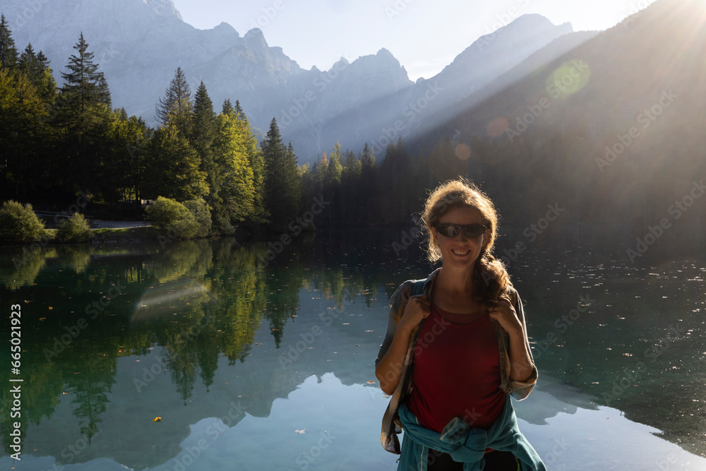 Female Caucasian Adult Tourist in front of a beautiful glacial lake in backlit of Julian Alps