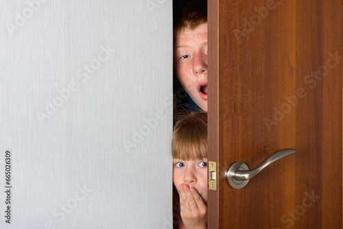 The children, a brother and a sister, peek curiously from behind the door of the room.