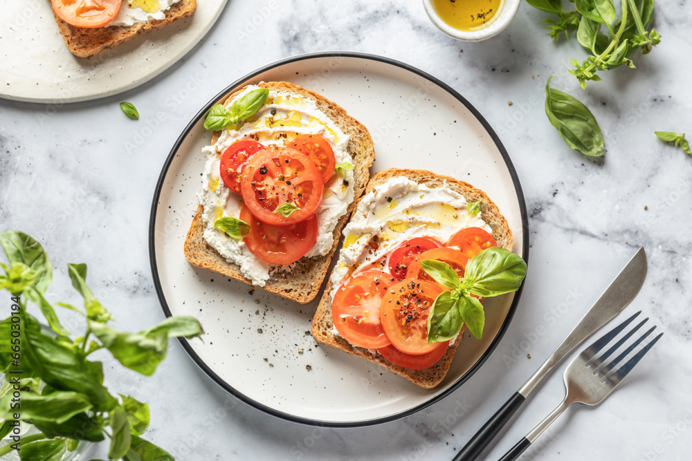 Sandwiches with tomatoes, cream cheese, olive oil and basil on a plate on white marble background. Traditional italian mediterranean food. Top view Sandwiches with tomatoes, cream cheese, olive oil and basil on a plate on white marble background. Traditional italian mediterranean food. Top view