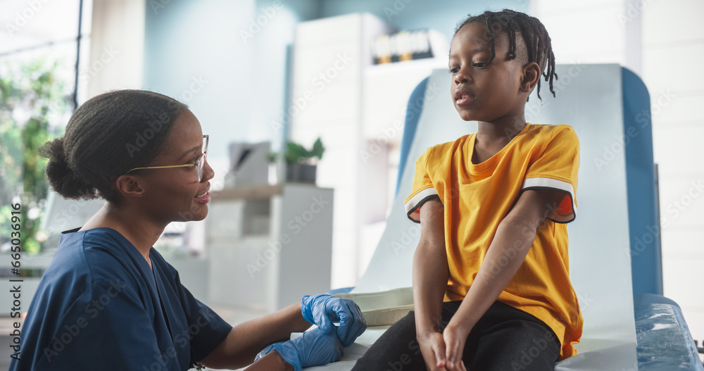 Obraz premium African Boy Sitting In The Chair In Hospital, Talking To Female Black Nurse. Professional Woman Listening To Young Man's Symptoms, Gives Advice On Proper Treatment. Public Healthcare Concept.