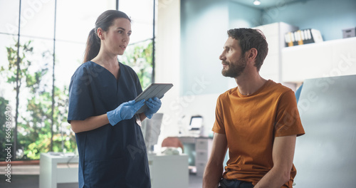 Caucasian Man Sitting In The Chair In Bright Hospital And Listening To Female Nurse With Tablet Computer. Professional Woman Explaining Possible Side Effects After Vaccination Or Medicine Injection.