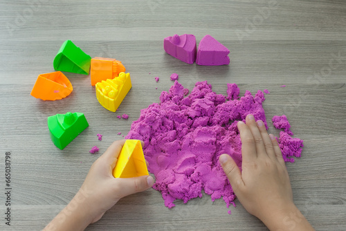 Little girl playing with bright kinetic sand at table indoors, closeup