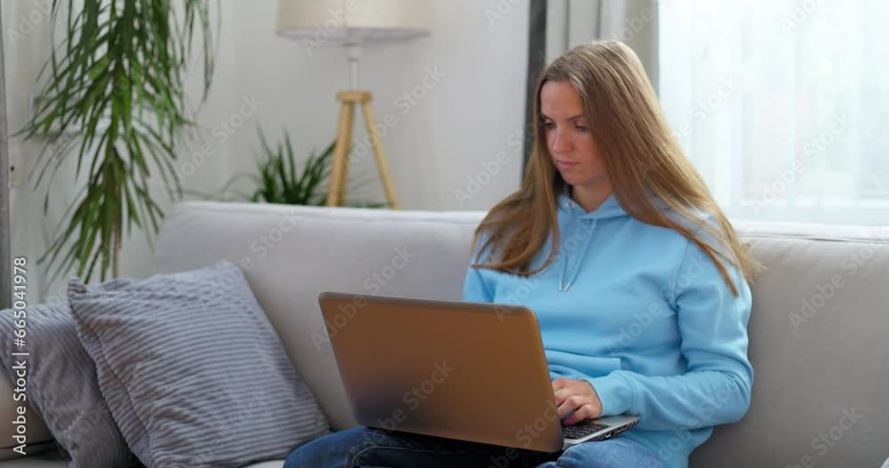 Woman sitting on sofa using laptop looking at screen typing message on computer Woman sitting on sofa using laptop looking at screen typing message on computer