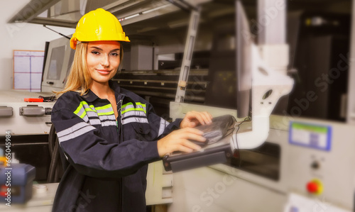 Smart female worker wearing safety helmet operates keyboard controlling computerized automated logo printing machine modern corrugated cardboard manufacturing logistics factory room. 