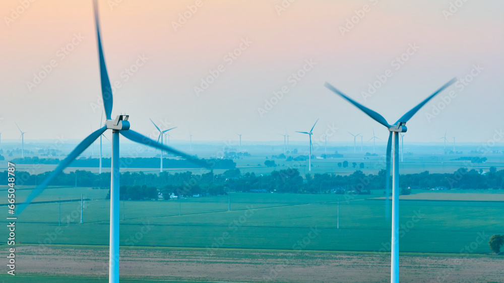 Wind turbines caught in motion on hazy morning with soft pink sky aerial