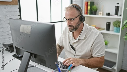 Handsome young business worker stressed, taking headphones off at the chaotic office environment photo