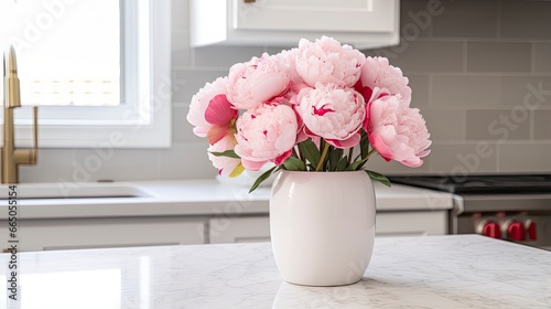 A white vase full of pink flowers is sitting on counter.