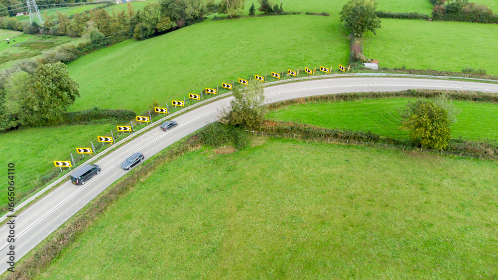 Sharp bend in a road with Chevron warning signs. Aerial view from above. Road safety. Cars are seen driving around the bend. Stunning countryside background. Road safety. Sharp bend in a road with Chevron warning signs. Aerial view from above. Road safety. Cars are seen driving around the bend. Stunning countryside background. Road safety.