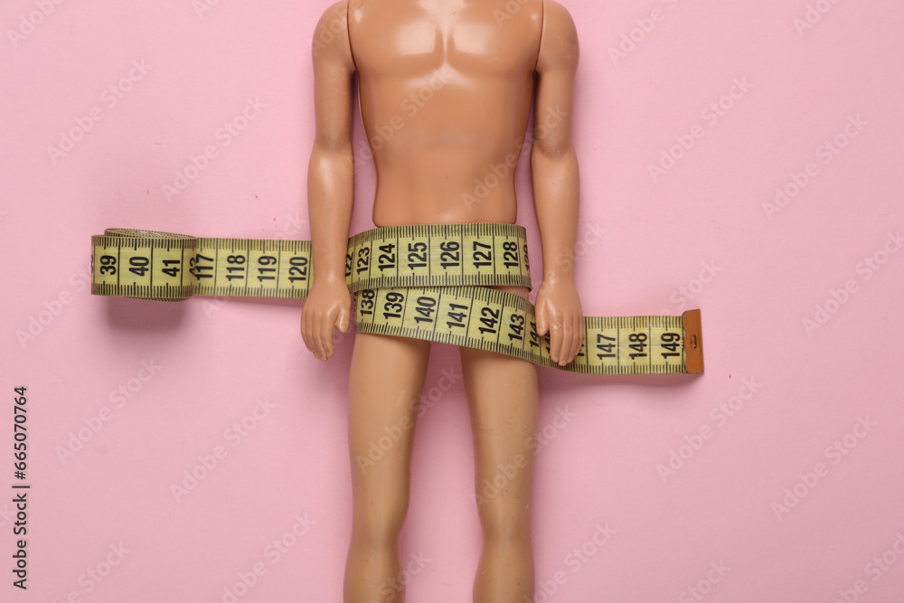 Naked male doll wrapped in measuring tape on a pink background - obrazy, fototapety, plakaty 