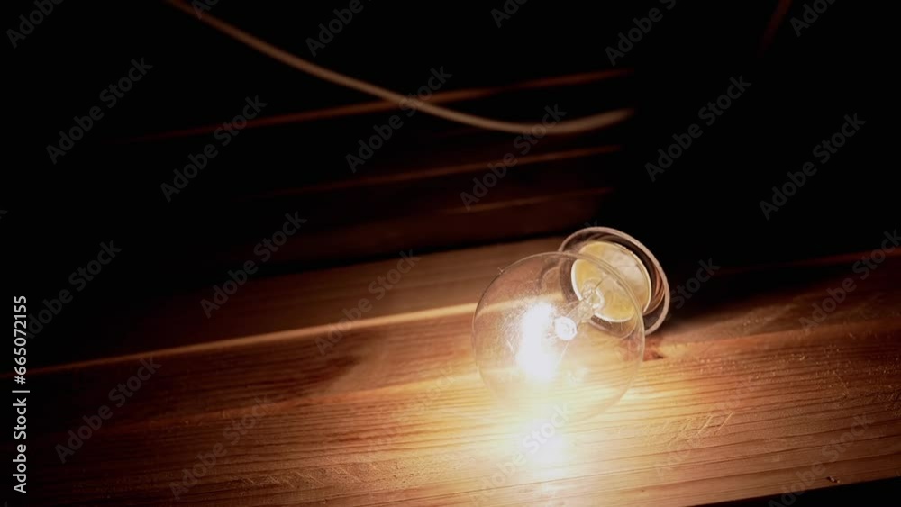 Hand Places an Incandescent Light Bulb on a Wooden Desk in a Dark Smoky Room. Dusty switched-on old Edison tungsten bulb shines a bright yellow light over a table in a dark room. Texture. Close up. Hand Places an Incandescent Light Bulb on a Wooden Desk in a Dark Smoky Room. Dusty switched-on old Edison tungsten bulb shines a bright yellow light over a table in a dark room. Texture. Close up.