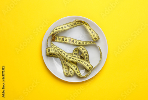 Plate with a measuring tape on a yellow background. Weight loss, diet concept