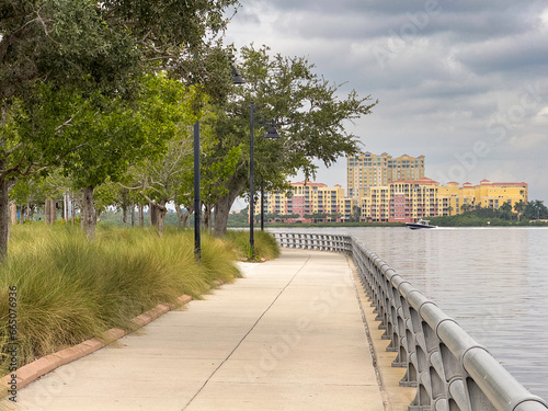 Perspective of municipal riverwalk in Bradenton, Florida, with view of speedboat passing by condominiums along Manatee River, on a cloudy afternoon at the end of September