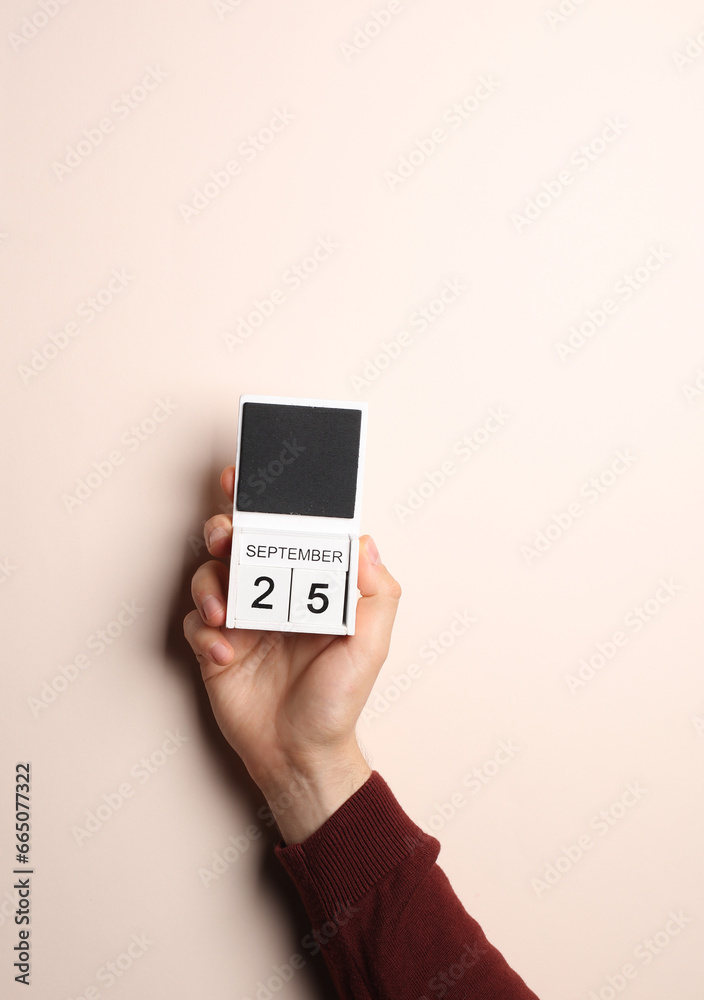 Man's hand in sweater holds block calendar with the date september 26 on a beige background Man's hand in sweater holds block calendar with the date september 26 on a beige background