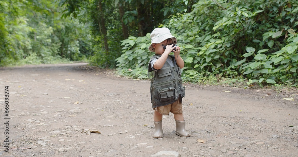 Fototapeta premium Happy Tourist cute little Asian toddler daughter kid girl using binoculars watching animals in the forest natural background, adventure explorer camping travel trip Learning about Nature