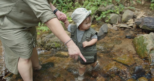happy family mother holding hand cute little Asian toddler daughter walking in mountain river water creek Learning about Nature in the rainforest, adventure explorer camping travel trip