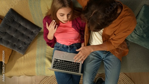 Top view capturing a young couple sitting on the couch, hugging and talking, looking at the laptop screen as if they are searching for something online. photo