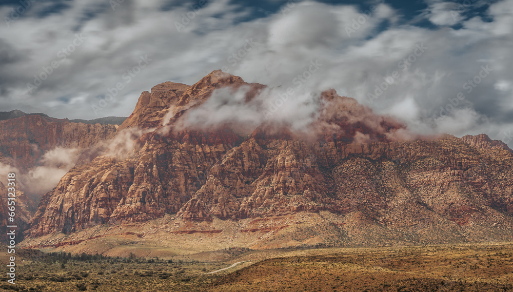 Landscape of Redrock National Park in the State of Nevada, United States. You can see the desert valley and the enormous red rock mountains, as well as the storm clouds in the sky.