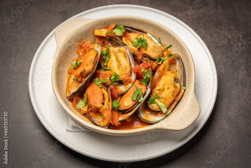 Mediterranean seafood dish of mussels stewed in sauce and herbs in a plate on a textured marble background.