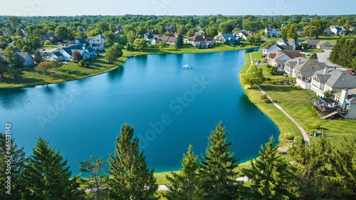 Low aerial with tree top view of large pond with water fountain and rich neighborhood