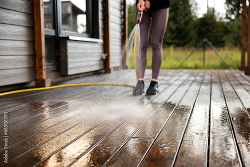 Woman washes a wooden terrace before painting it in her modern private house © Uldis Laganovskis