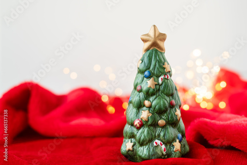 New Year's location with a green toy fir tree standing on a red blanket against a bokeh background with a garland of lights. Place for an inscription. photo