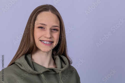 Young girl with smile shows white teeth with braces. Gray background.