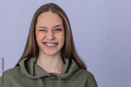 Young girl with smile shows white teeth with braces. Gray background.