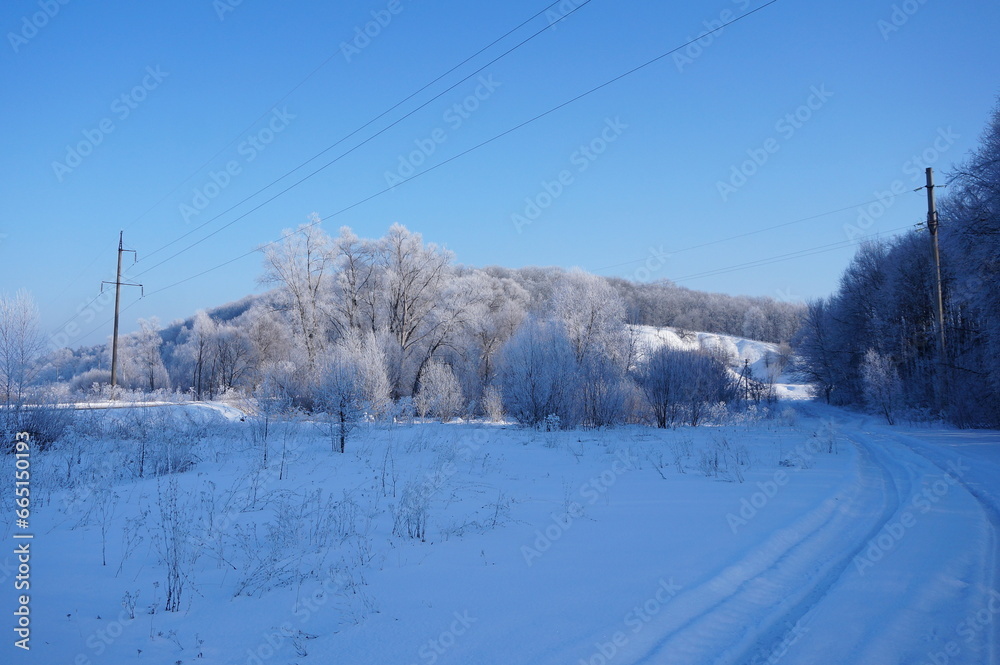 Winter rural landscape. Road covered in snow in the forest. Trees in frost, frosty day. Winter rural landscape. Road covered in snow in the forest. Trees in frost, frosty day.